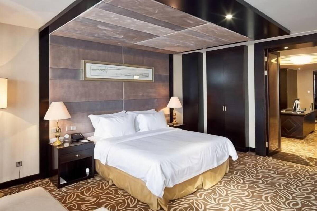 A hotel room with a large bed, two bedside tables with lamps, a framed artwork on the wall, and a patterned carpet.