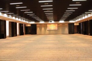 Una habitación amplia con alfombra, techo alto y luminarias rectangulares.