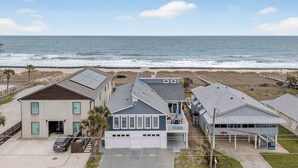 A coastal building with a garage, a balcony, and a view of the ocean. - Sea Monster by Carolina Getaway - 6BR Remodeled Oceanfront Home w/ Heated Pool (Kure Beach)