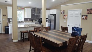Una cocina moderna con armarios blancos, un refrigerador de acero inoxidable y un comedor con mesa y sillas de madera.