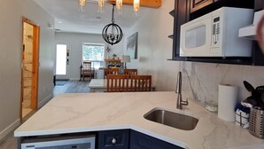 A kitchen with a built-in dishwasher, a microwave, and a sink. There is a dining area with a table and chairs in the background. - ❤ Modern Rustic 2BR 2BTH Mountain Chalet close to Banff (Harvie Heights)