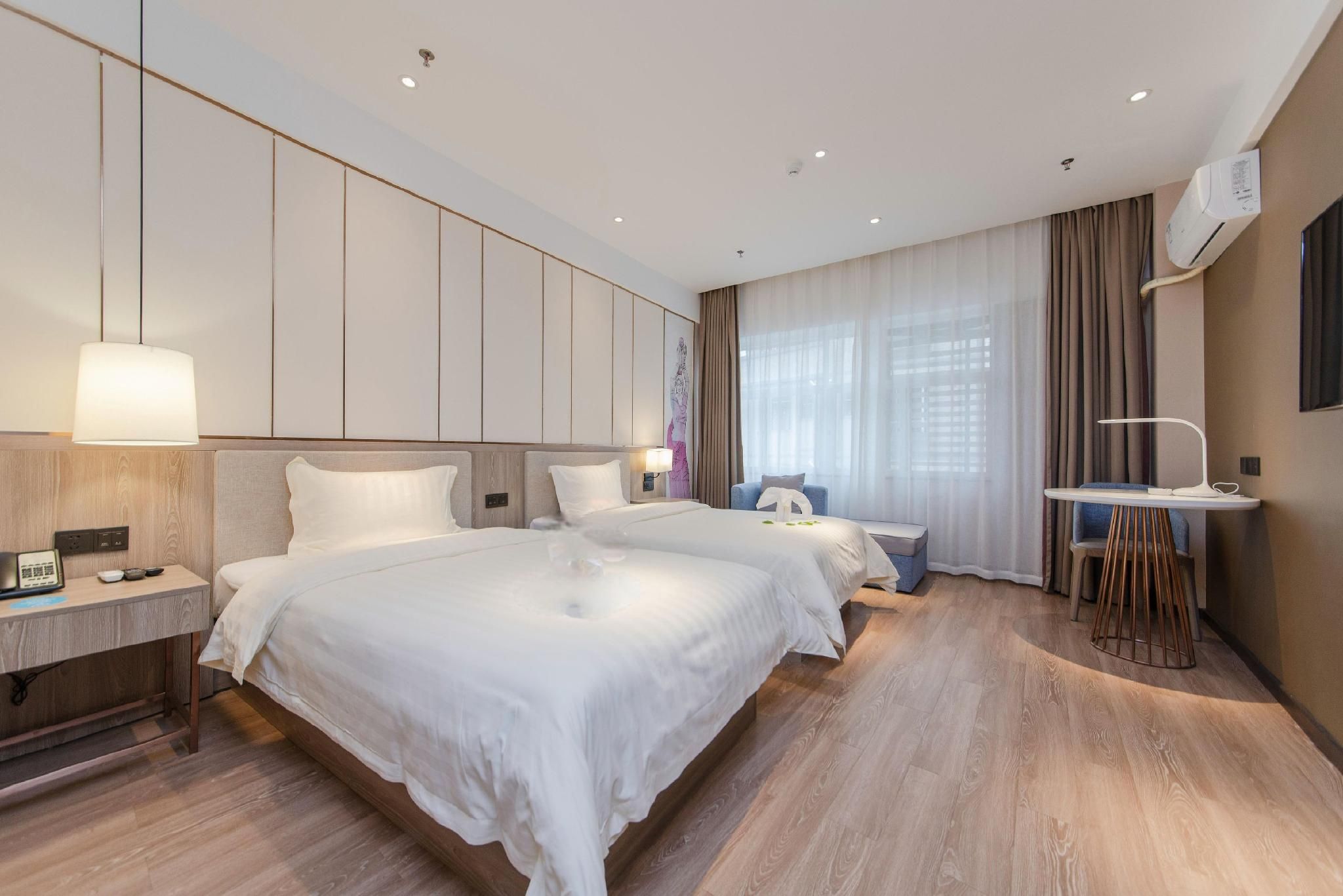 A hotel room with two beds, a desk, a chair, and a small table.