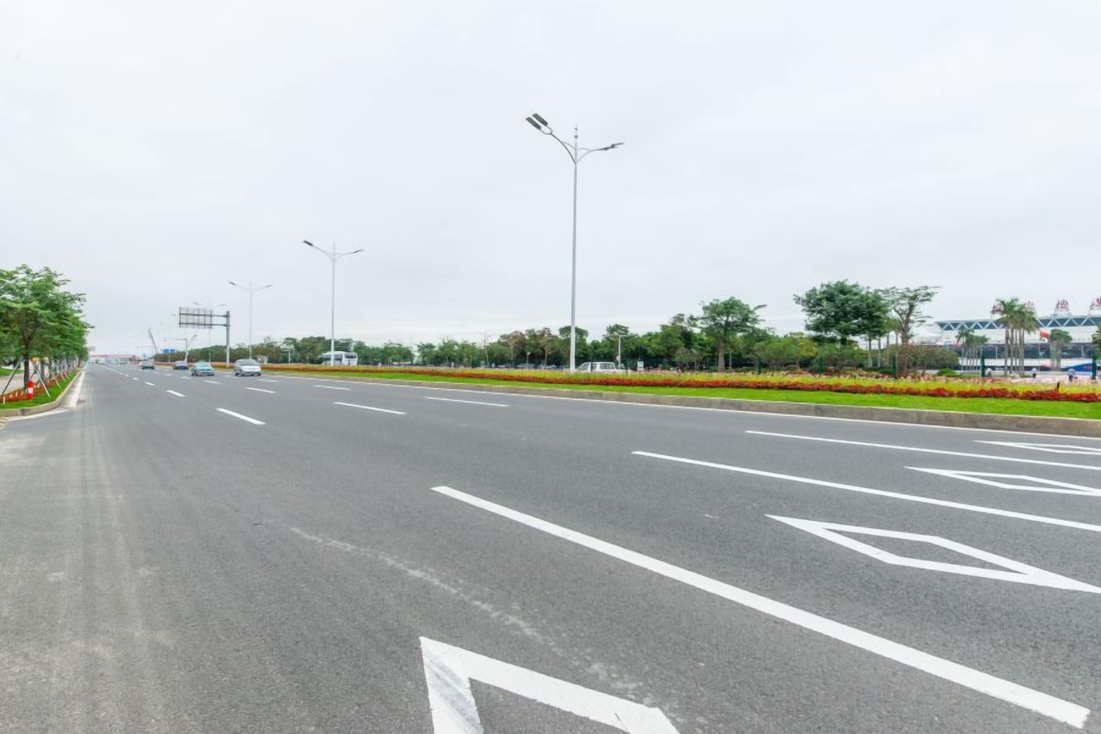 A multi-lane road with directional arrows, streetlights, and a landscaped median with trees and flowers.