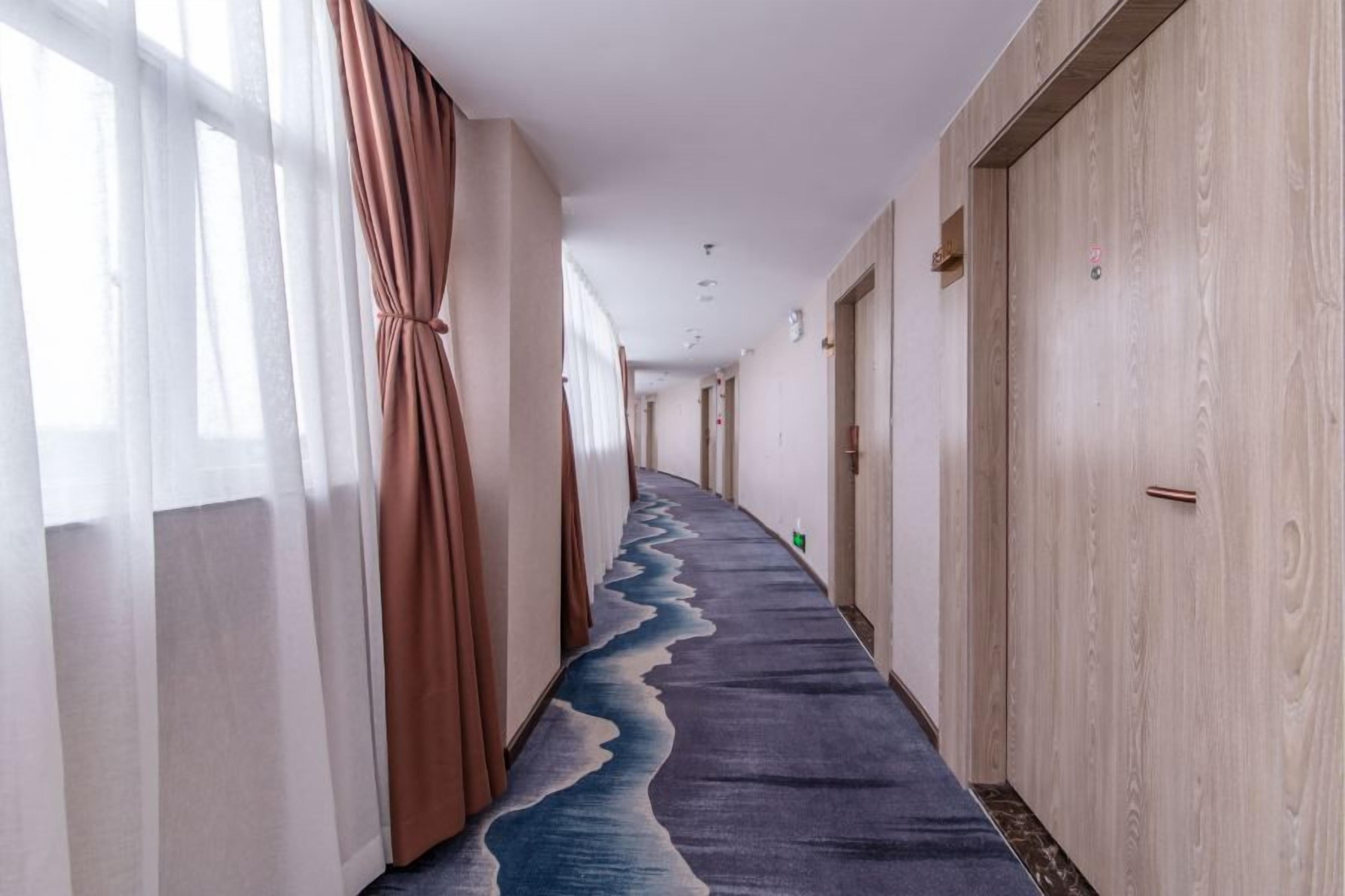 A hotel corridor with a carpeted floor, wooden doors, and a window with curtains.