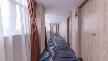 A hotel corridor with a carpeted floor, wooden doors, and a window with curtains.