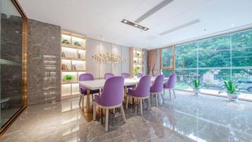 A modern dining area with a marble floor, purple chairs, a white table, and a view of greenery through large windows.