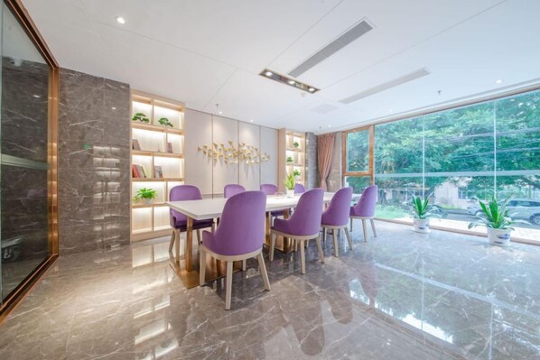 Un espace de restauration moderne avec un sol en marbre, des chaises violettes, une table blanche et une vue sur la verdure grâce à de grandes fenêtres.