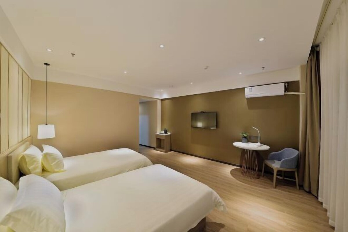 Ein Hotelzimmer mit zwei Betten, einem kleinen runden Tisch mit einem Stuhl, einem an der Wand montierten Fernseher und einer Klimaanlage.