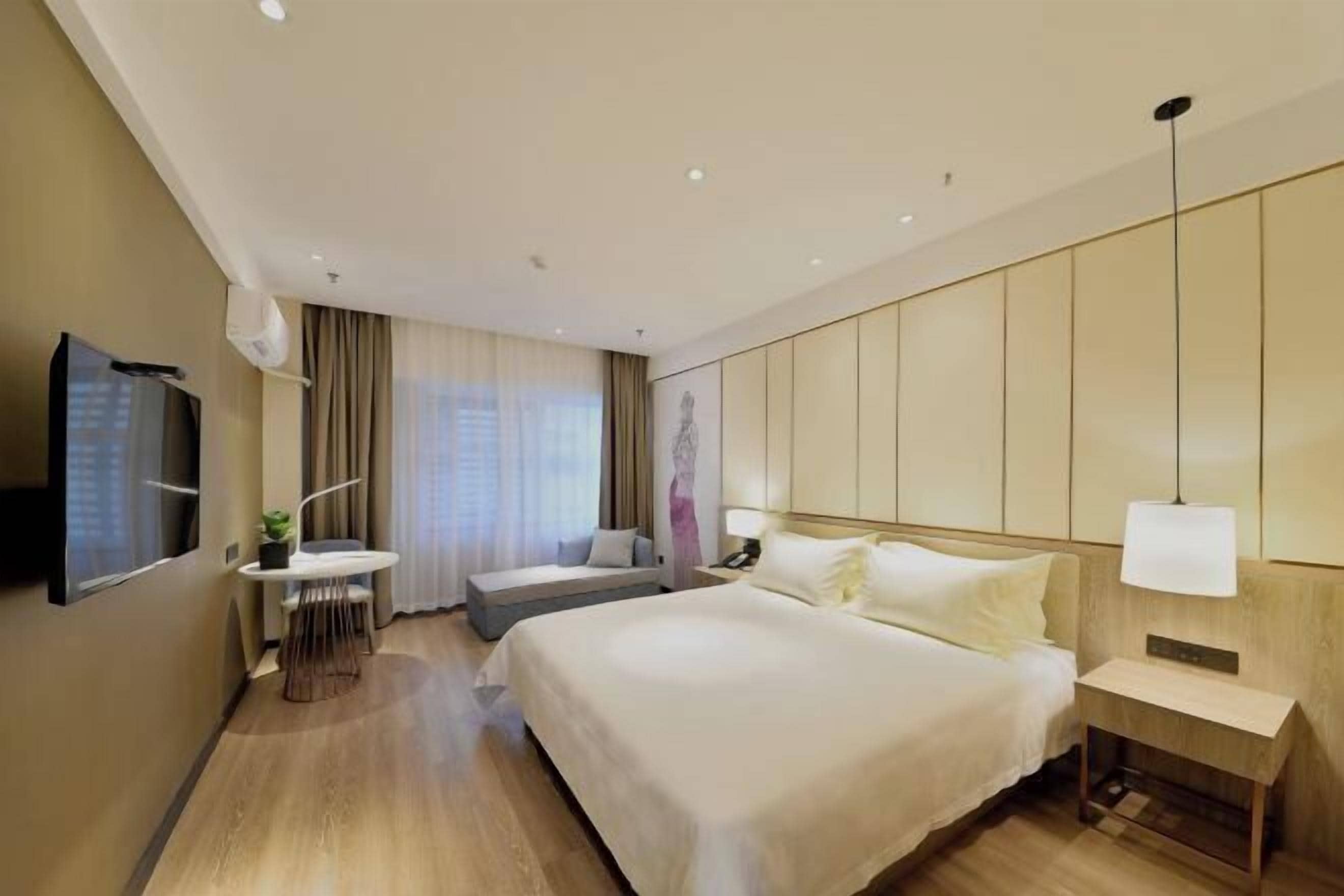A hotel room with a large bed, a desk with a chair, a TV, and a bedside table with a lamp.