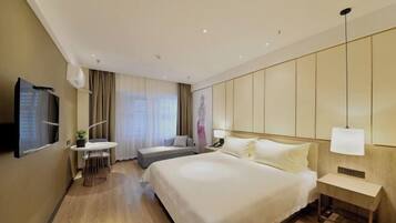 A hotel room with a large bed, a desk with a chair, a TV, and a bedside table with a lamp.