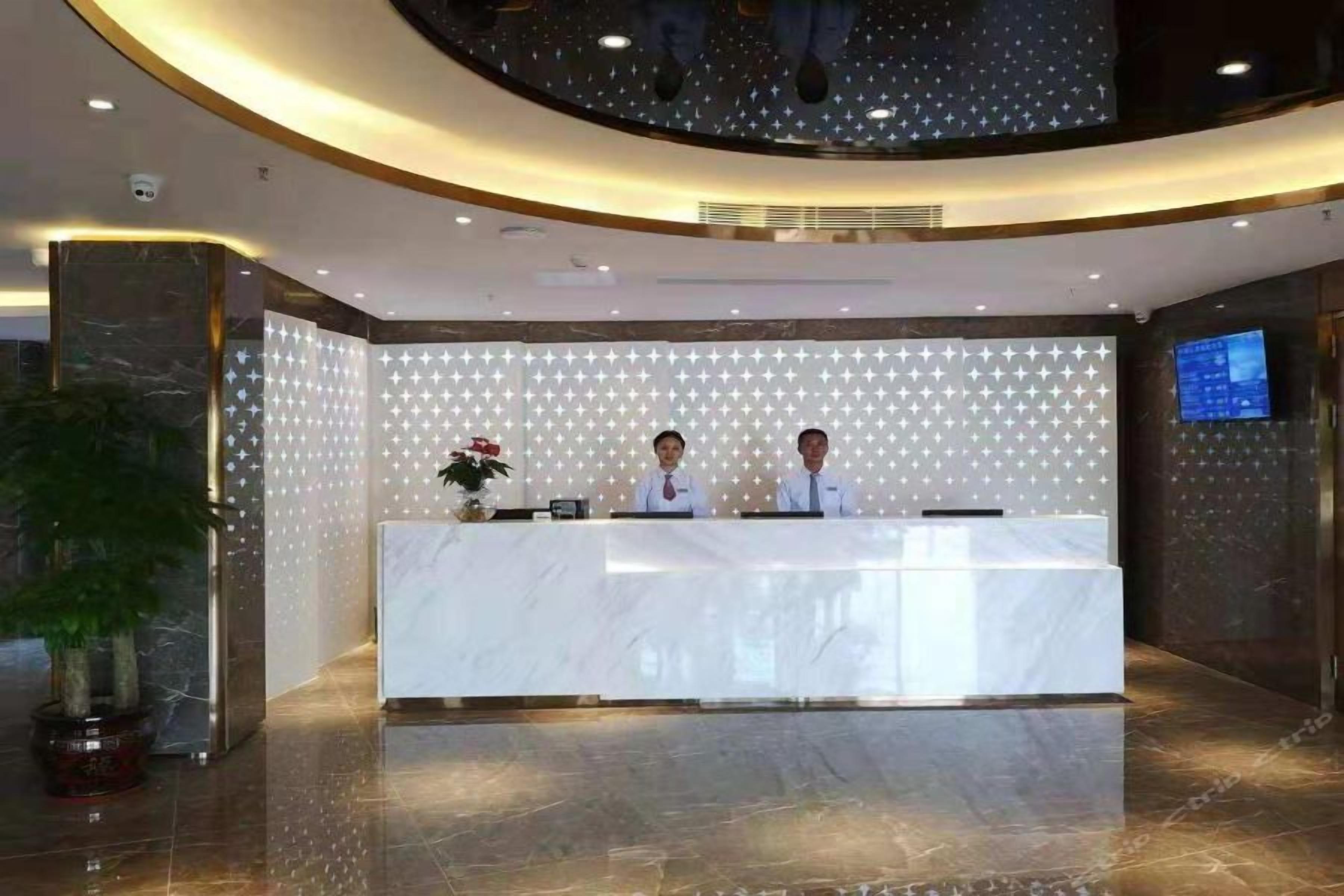 A reception desk with two staff members, a marble counter, a star-patterned wall, a potted plant, and a television screen.