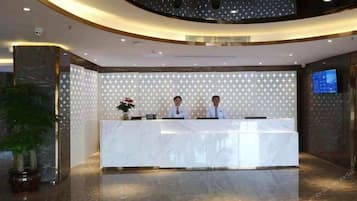 A reception desk with two staff members, a marble counter, a star-patterned wall, a potted plant, and a television screen.