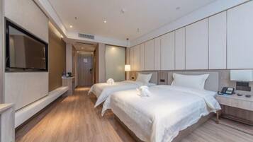 A hotel room with two beds, a TV, a bedside table with a lamp, and a wooden floor.