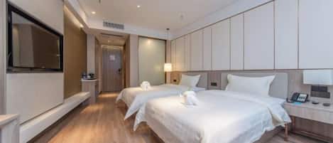 A hotel room with two beds, a TV, a bedside table with a lamp, and a wooden floor.