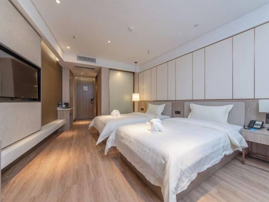 Habitación de hotel con dos camas, un televisor, una mesita de noche con lámpara y suelo de madera.
