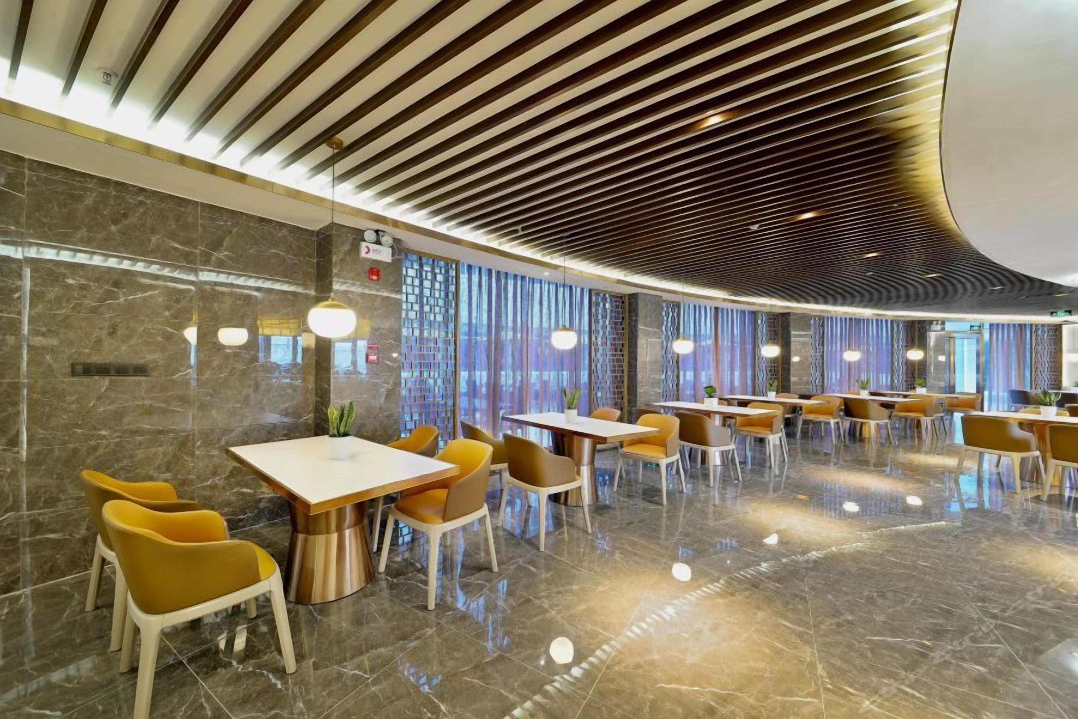Un restaurante moderno con un diseño elegante, que presenta un piso de mármol pulido, muebles contemporáneos y un techo con patrones lineales.