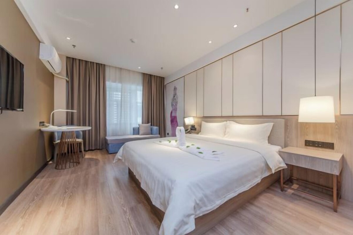 Ein modernes Hotelzimmer mit einem großen Bett, einem Nachttisch und einem kleinen Schreibtisch mit Stuhl.