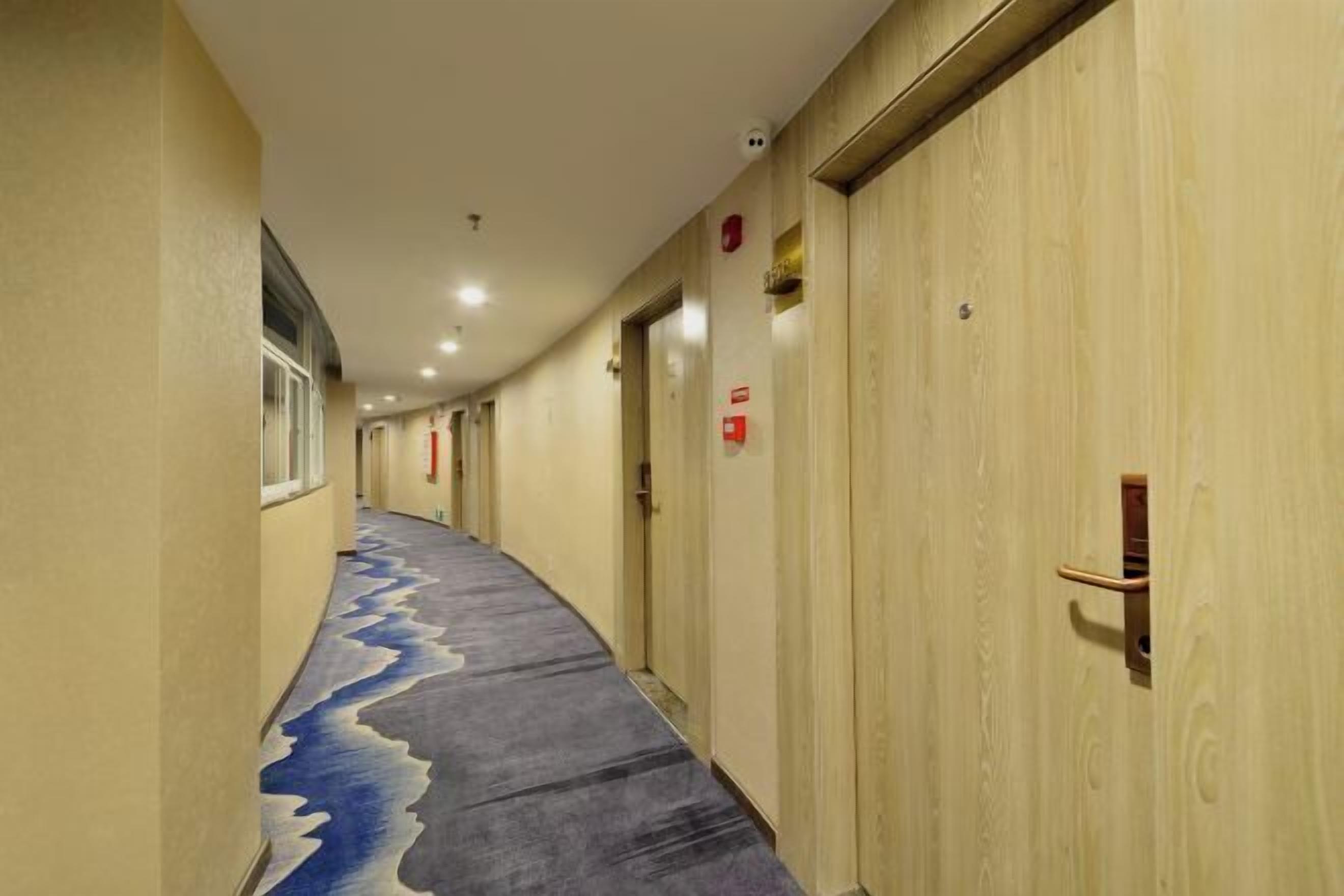 Un pasillo de hotel con puertas de madera, una alfombra estampada e iluminación empotrada en el techo.