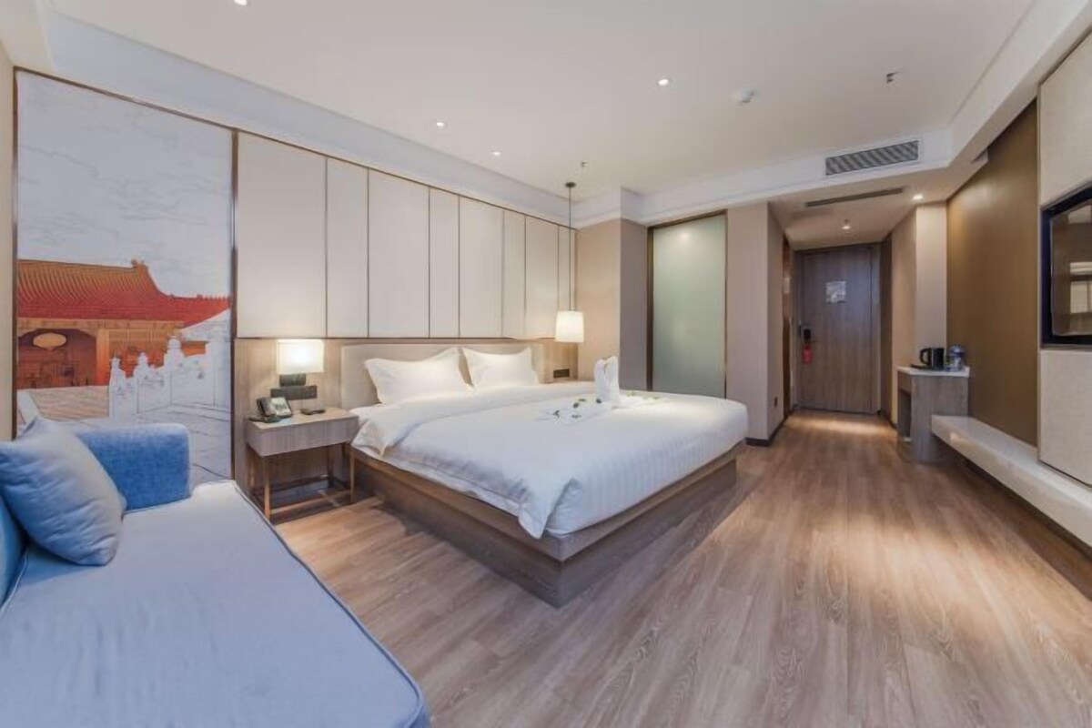 Ein modernes Hotelzimmer mit einem großen Bett, Nachttischen, einem Schreibtisch und einem an der Wand befestigten Fernseher.