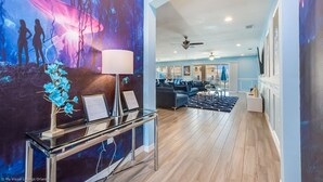 Una sala de estar moderna con un mural grande, una mesa de centro de vidrio y un ventilador de techo.