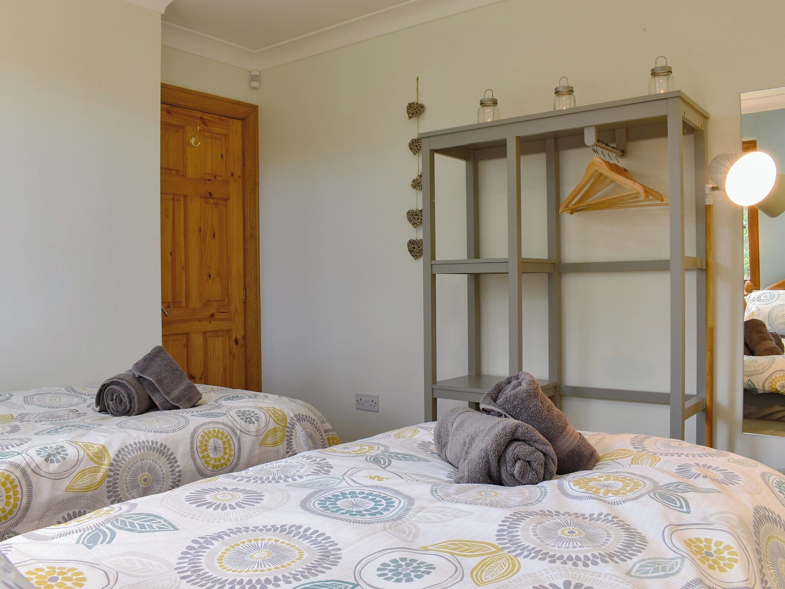 A hotel room with two beds, a wooden door, a metal wardrobe, and a mirror with a light.
