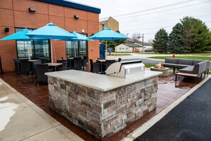 Un patio al aire libre con asientos de piedra, una parrilla y sombrillas azules.