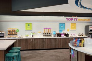 Un espace dédié au petit-déjeuner, avec un comptoir où sont exposés divers aliments et une pancarte indiquant : « PETIT-DÉJEUNER À VOLONTÉ ».