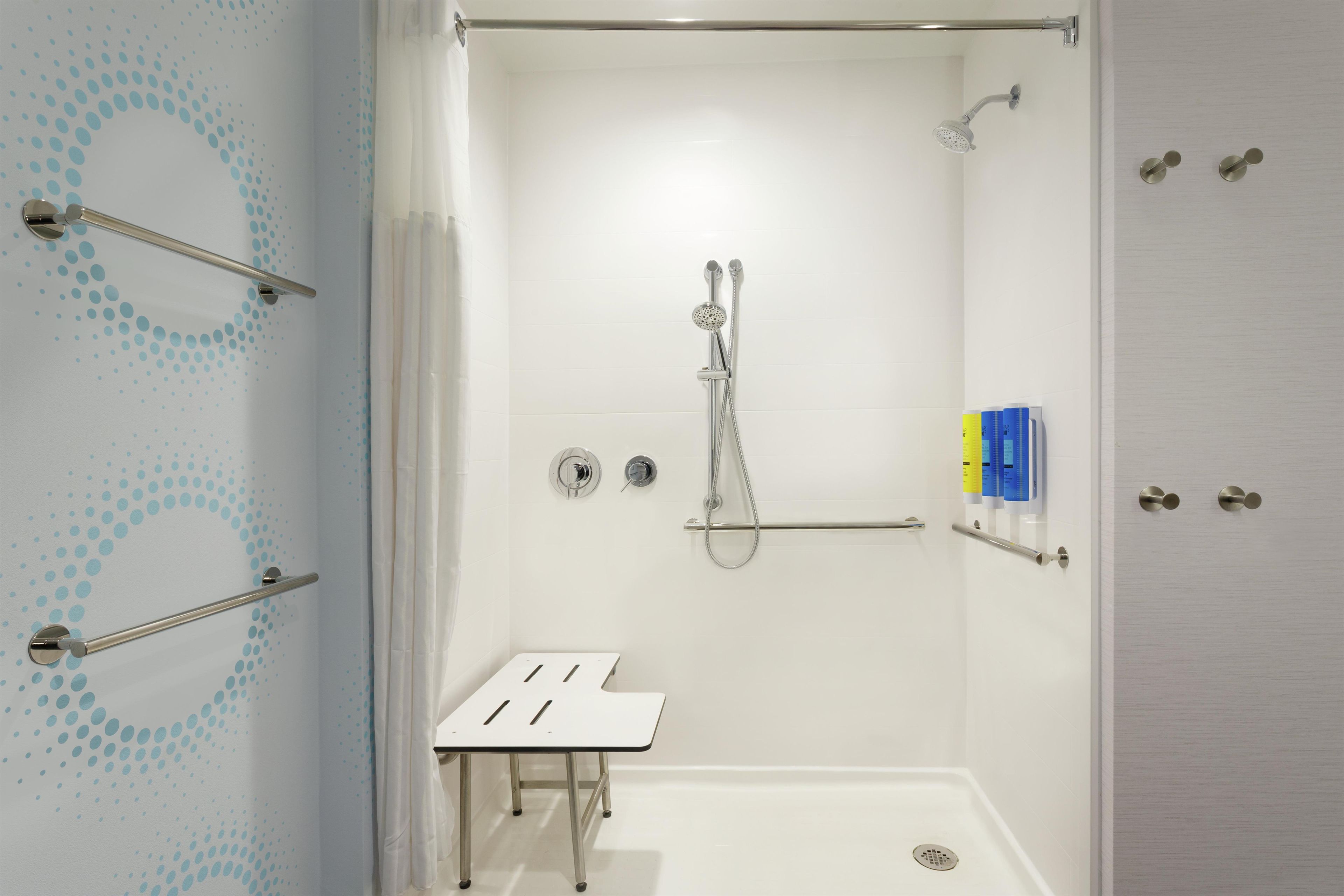 Área de banho com chuveiro manual, porta-toalhas e uma pequena mesa.