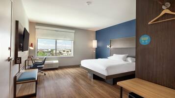 Quarto de hotel com cama, escrivaninha, cadeira, televisão, janela e sinalização de armazenamento.