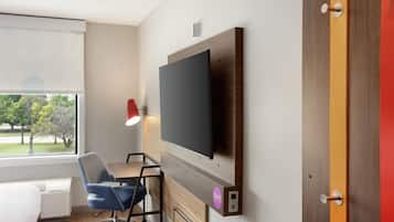 Une chambre d’hôtel moderne équipée d’un téléviseur à écran plat fixé au mur, d’un bureau avec une chaise, d’une fenêtre avec des stores et d’une porte dotée d’un cadre rouge.