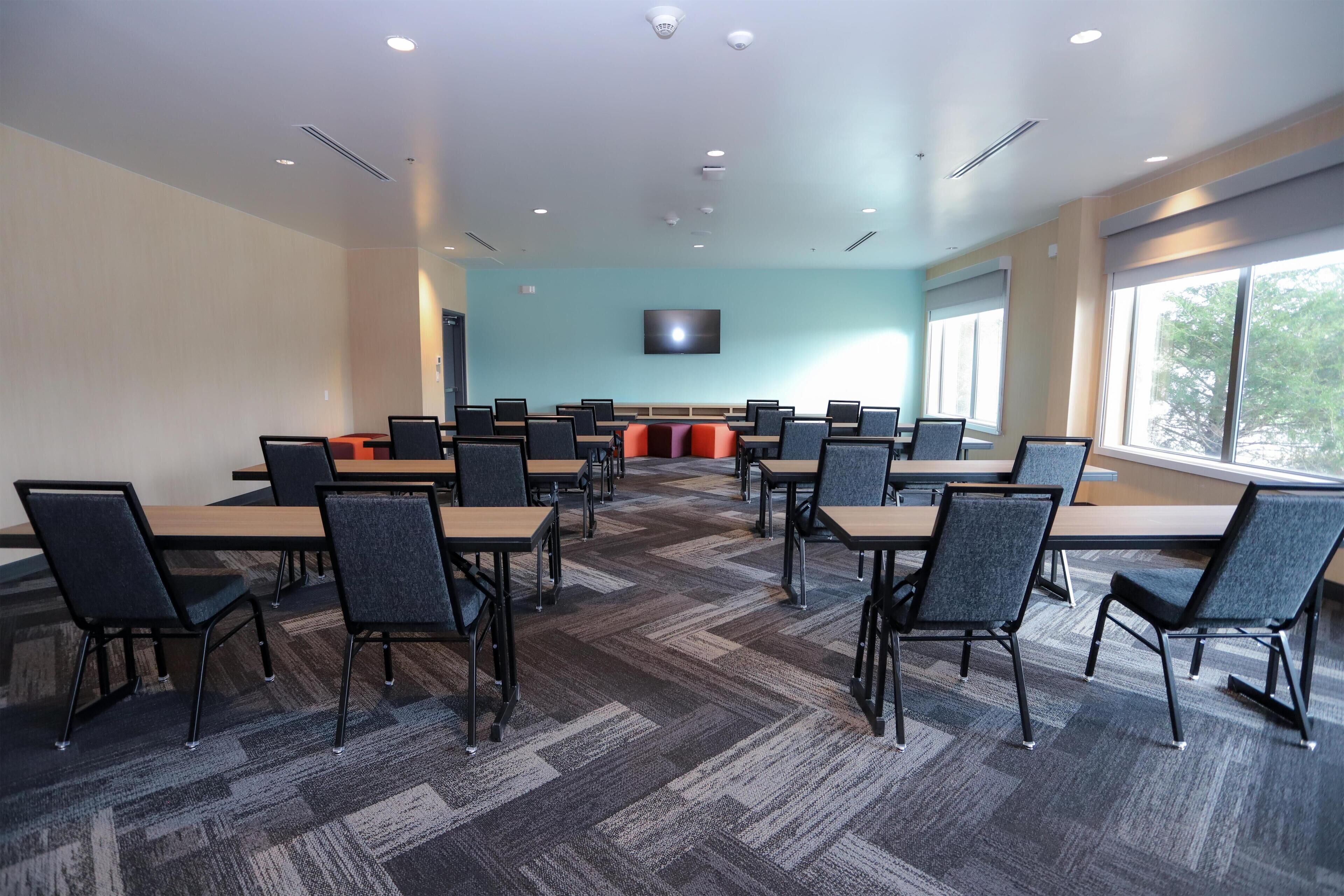 A conference room with a large table, chairs, a flat-screen TV, and a window.