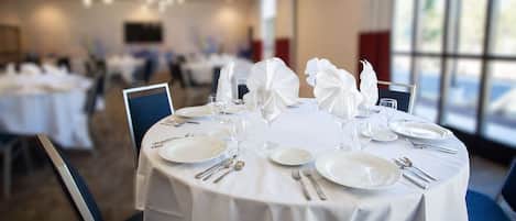 A dining area with round tables set for a meal, featuring white tablecloths, plates, cutlery, and folded napkins.