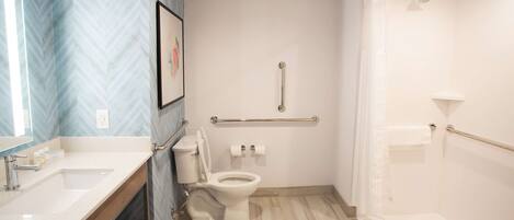 A modern bathroom with a white sink, toilet, and shower. It includes a handrail and a picture on the wall.