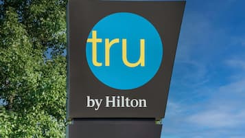 Un letrero con el logotipo 'tru by Hilton' sobre un cielo despejado y follaje verde.