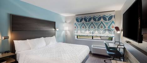 A modern hotel room with a large bed, a desk, a chair, a flat-screen TV, and a patterned wall.