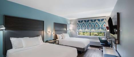 A hotel room with two beds, a desk, a chair, and a window with a view.