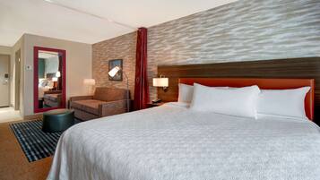 A hotel room with a large bed, a chair, a desk, and a mirror.