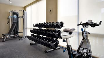 A gym with a stationary bike, dumbbells, and a weight machine.
