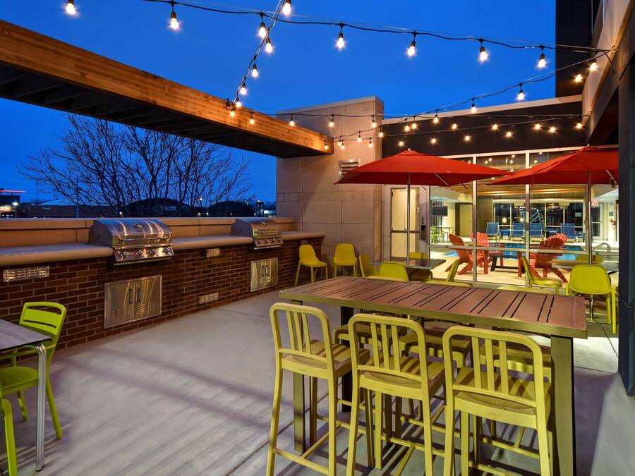 An outdoor patio with a barbecue grill, yellow chairs, and red umbrellas.