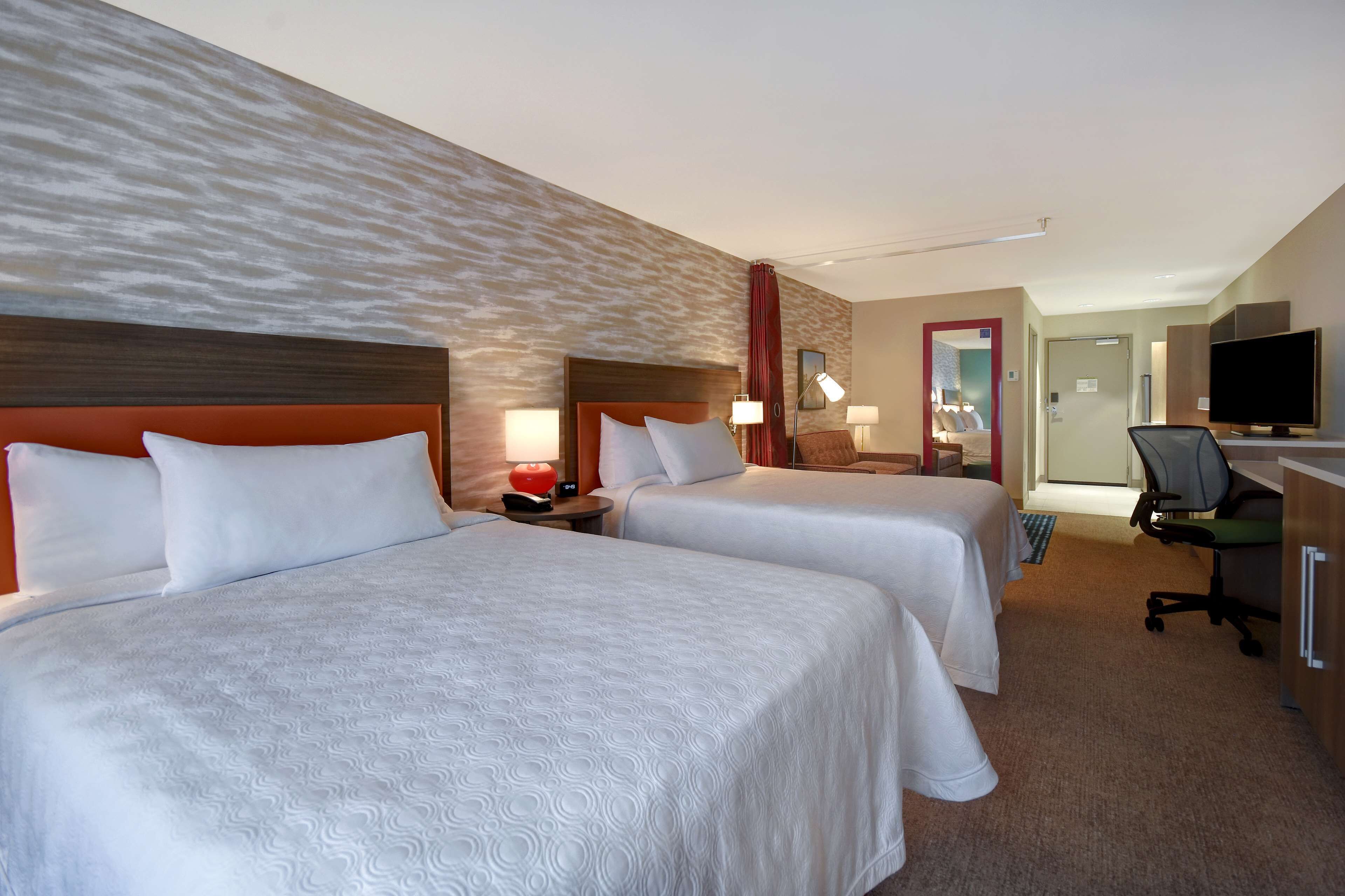A hotel room with two beds, a desk, a chair, a television, and a bathroom visible in the background.