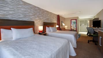 A hotel room with two beds, a desk, a chair, a television, and a bathroom visible in the background.
