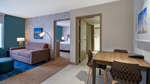 Ein Hotelzimmer mit einer Couch, einem Esstisch mit Stühlen, einer Lampe und einem Bett im Hintergrund.