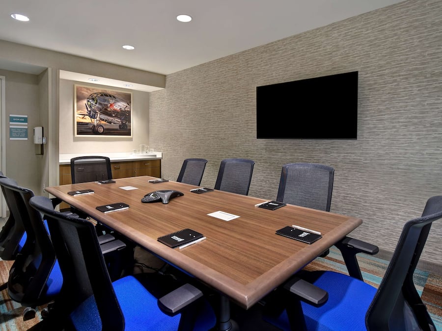A conference room with a long table, six chairs, a mounted TV, and a painting on the wall.