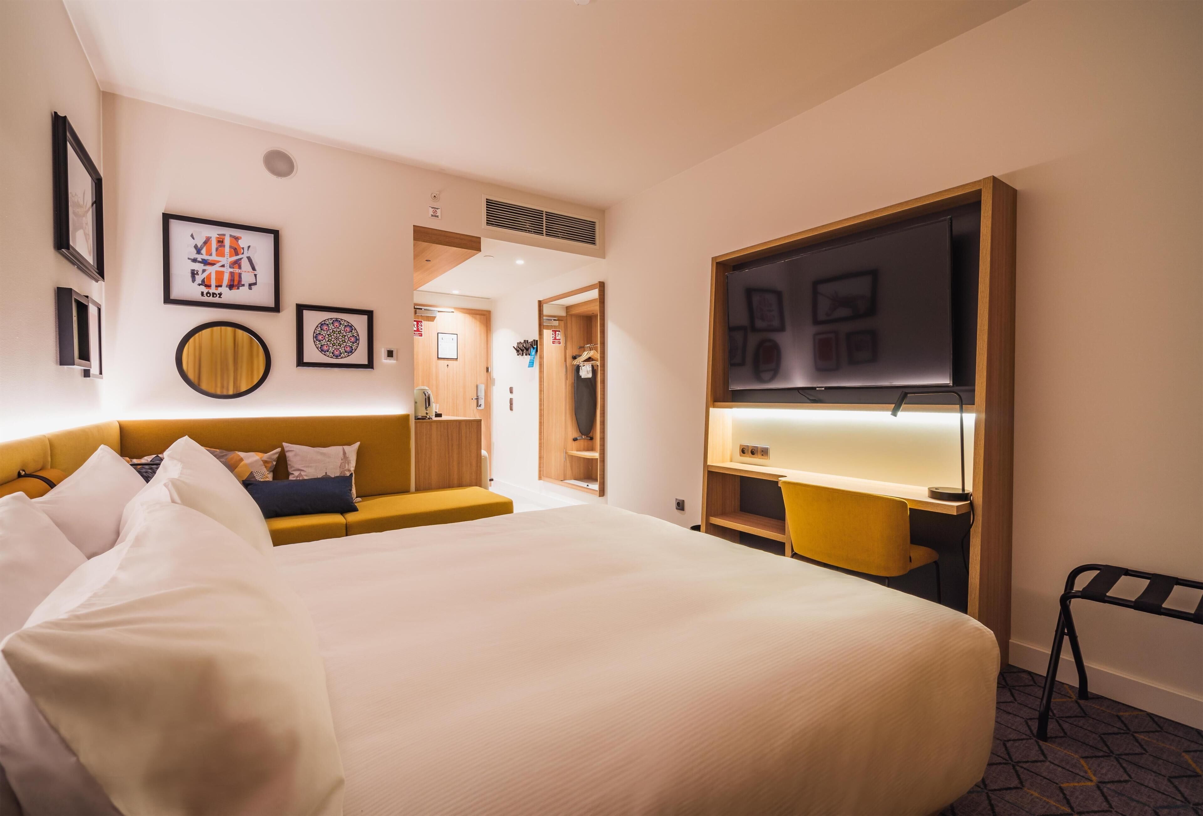 Habitación de hotel con una cama grande, un escritorio, una silla, un televisor y obras de arte en las paredes.