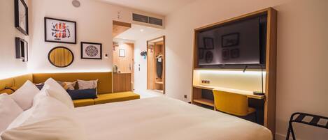 Habitación de hotel con una cama grande, un escritorio, una silla, un televisor y obras de arte en las paredes.