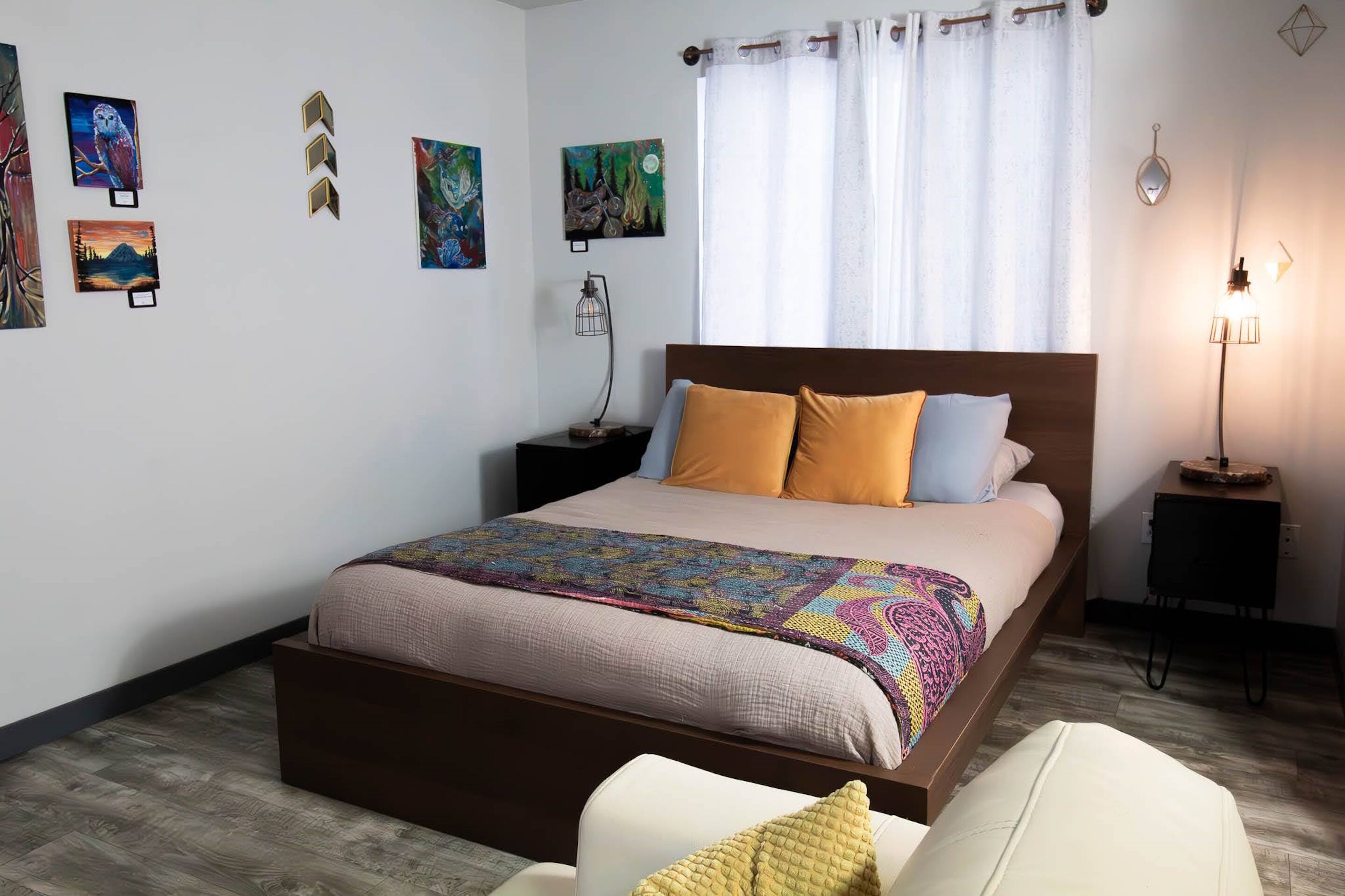 A neatly arranged bedroom with a large bed, a bedside table, a lamp, and artwork on the walls.