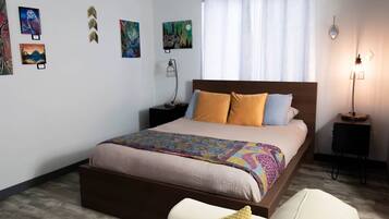 A neatly arranged bedroom with a large bed, a bedside table, a lamp, and artwork on the walls.