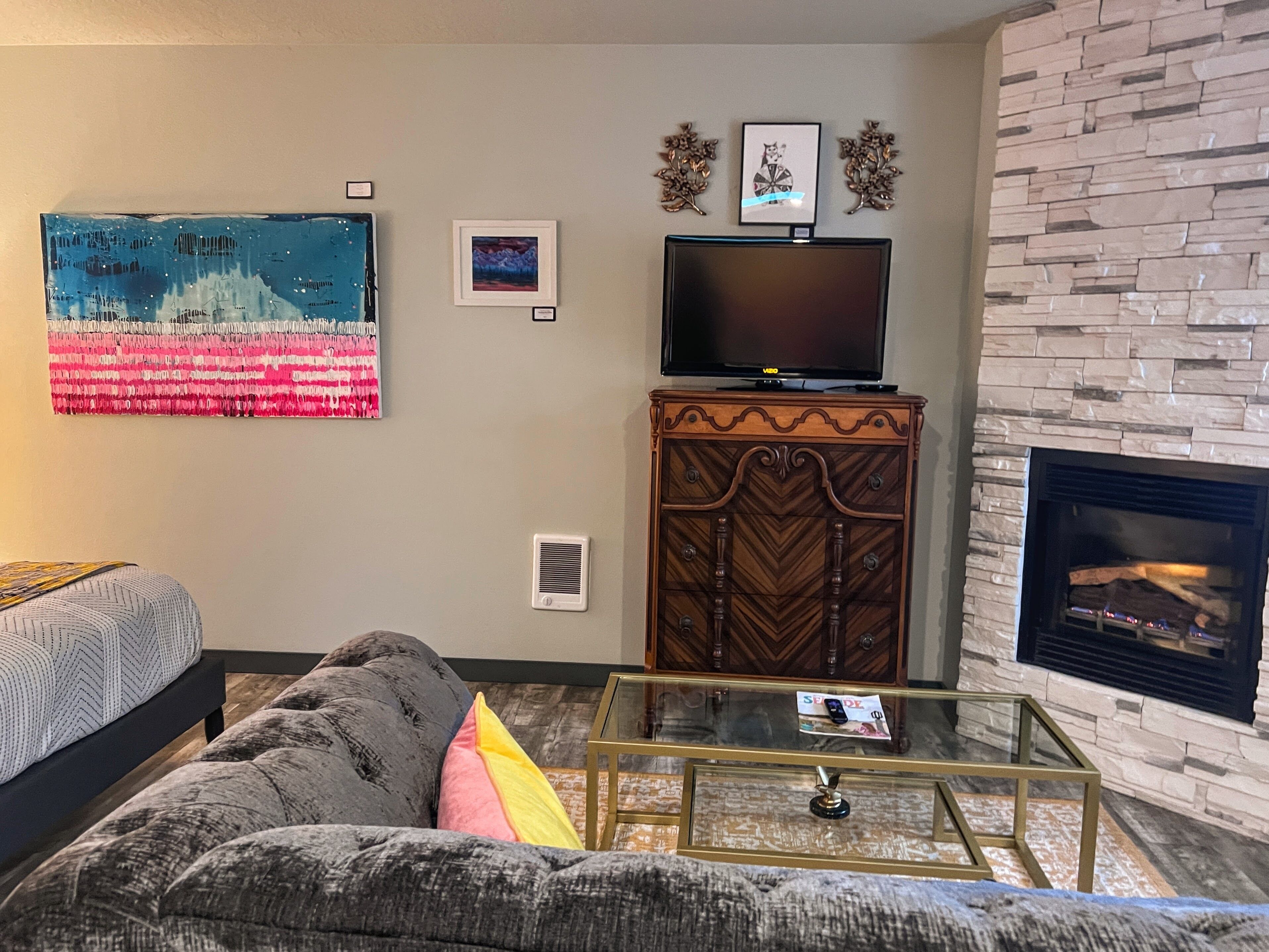 A living room with a sofa, a coffee table, a flat-screen TV, decorative wall art, and a stone fireplace.