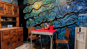 A kitchen with a wooden cabinet, a table with chairs, and a wall mural. - The Starry Night Inn (Seaside)