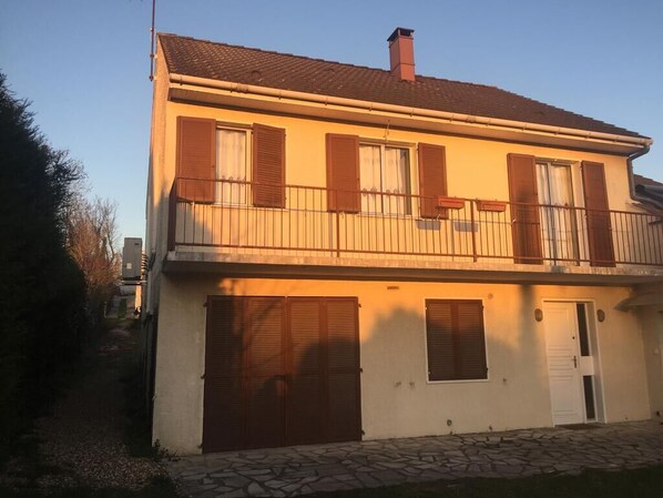 A two-story house with a balcony, shutters, and a stone pathway. - Appartement F3 à Pierrelaye (Pierrelaye)